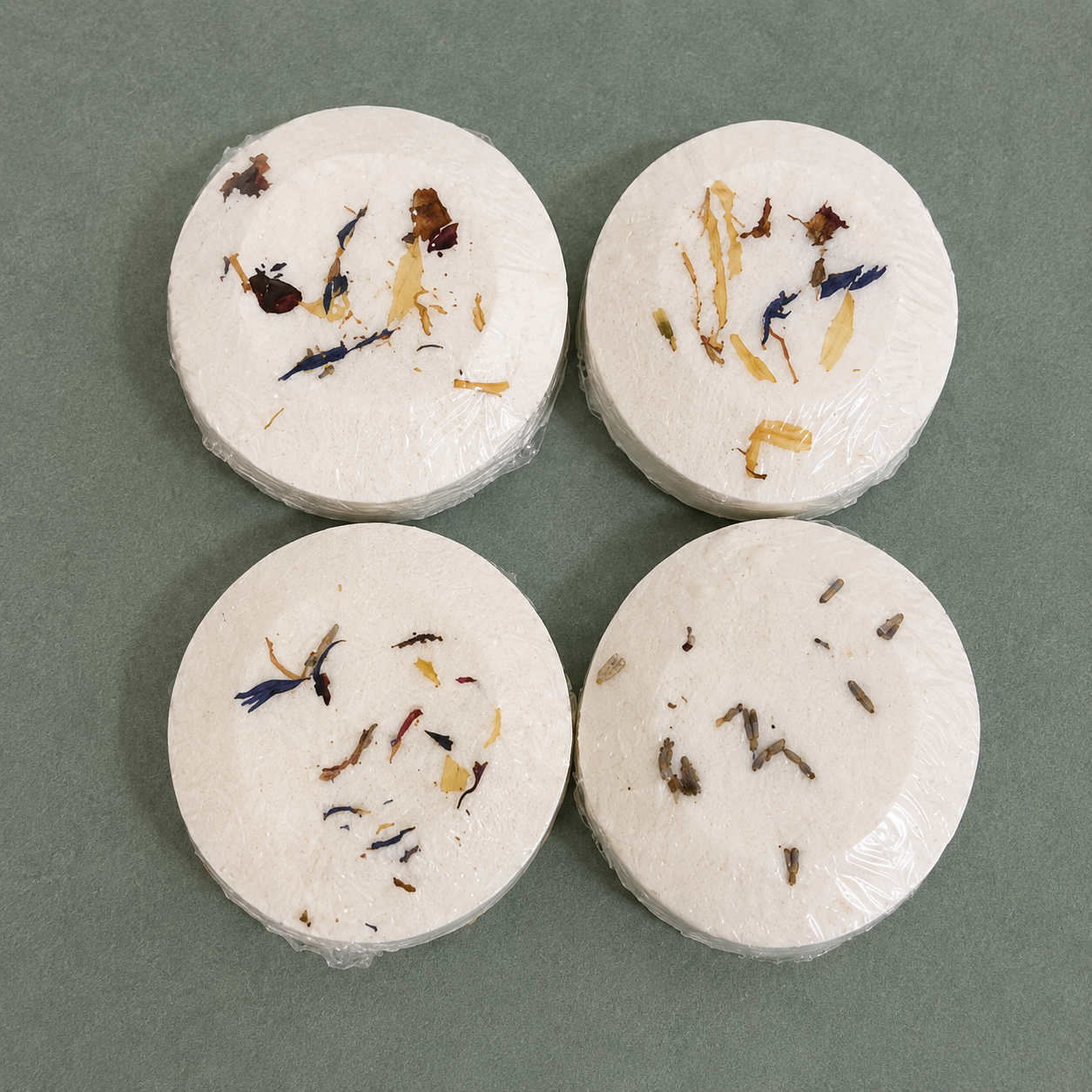 Four handcrafted aromatherapy shower steamers with dried botanicals on a sage green background, including Lavender, Balance, Headspace, and Deep Reset.